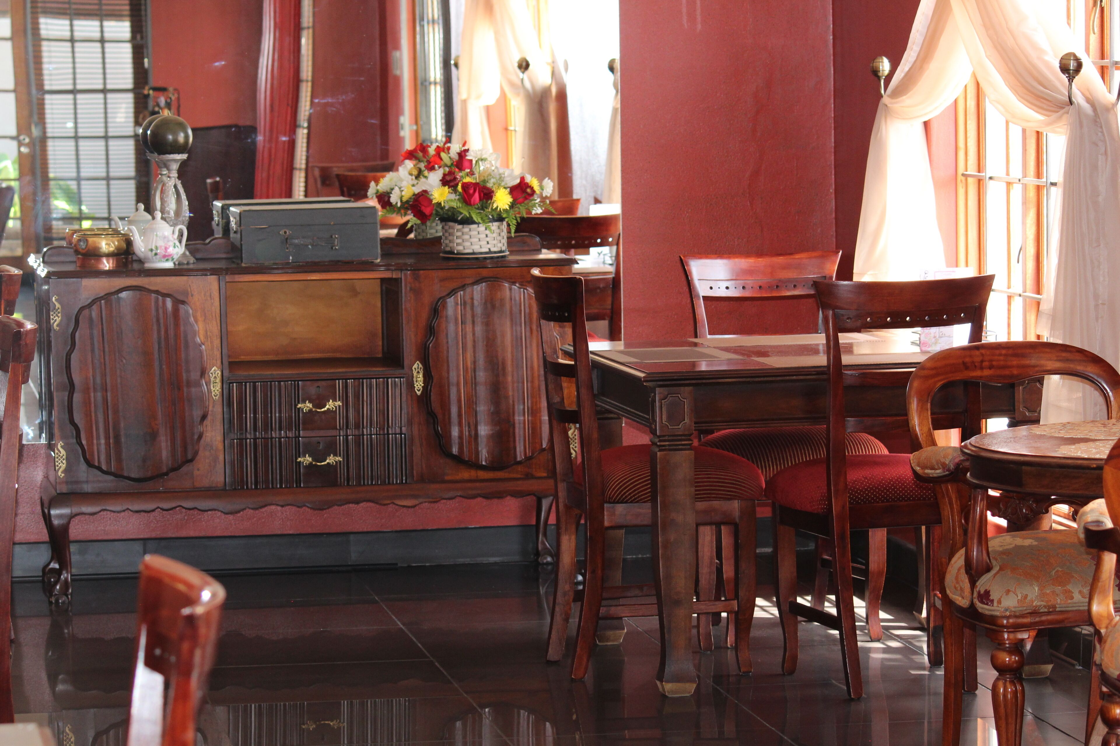 A traditional wooden dining table with chairs, a cabinet with drawers, and a vase with flowers on the table.