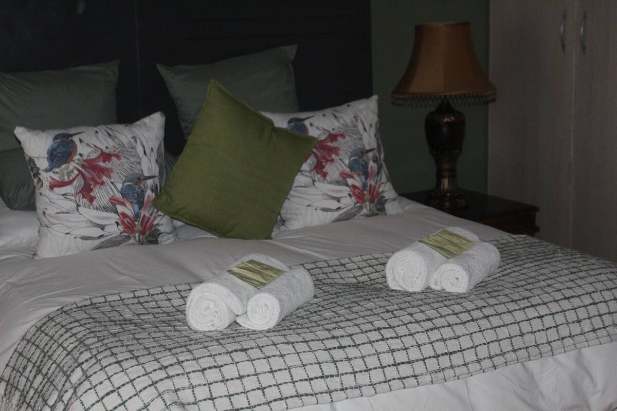 Una cama bien hecha con almohadillas florales, una colcha a cuadros y toallas enrolladas sobre la cama.