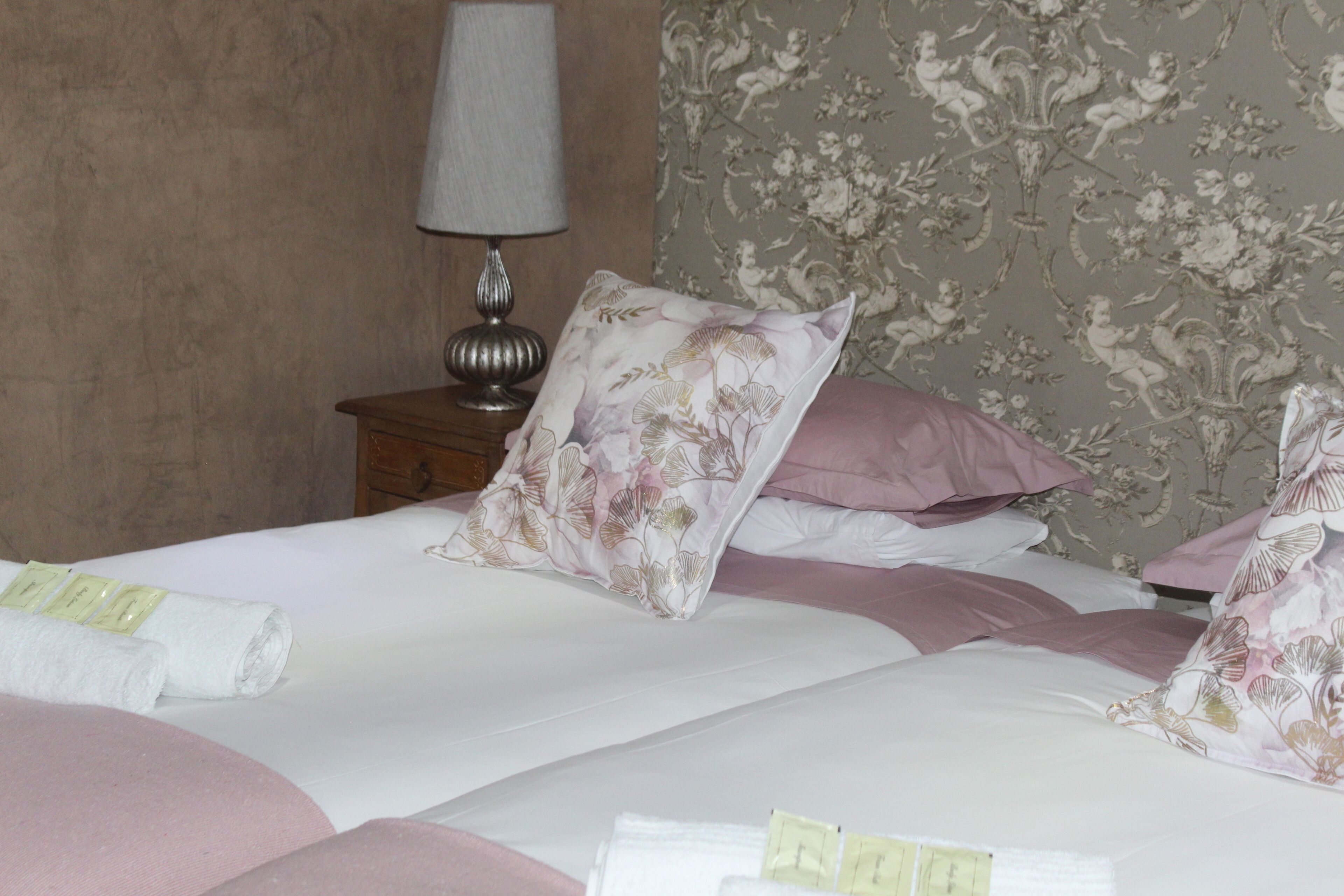 A neatly made bed with floral-patterned pillows and a rolled white towel on the side.
