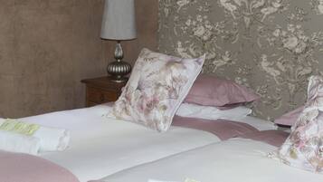 A neatly made bed with floral-patterned pillows and a rolled white towel on the side.