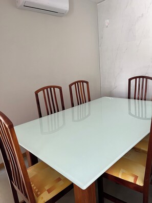 Conference room with a glass-top table and cushioned chairs, surrounded by a marble wall and air conditioning unit.