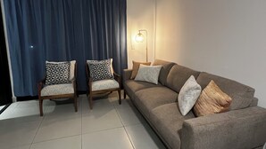 Ein Wohnzimmer mit einer Couch, zwei Sesseln, einer Lampe und einem großen Fenster mit Vorhängen.