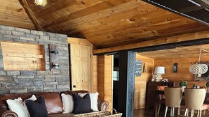 Ein gemütliches Wohnzimmer mit Steinwand, Holzboden und einer Essecke mit Tisch und Stühlen.
