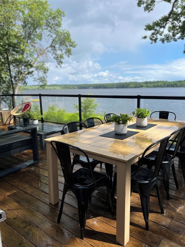 A wooden deck with a table and chairs, overlooking a lake.