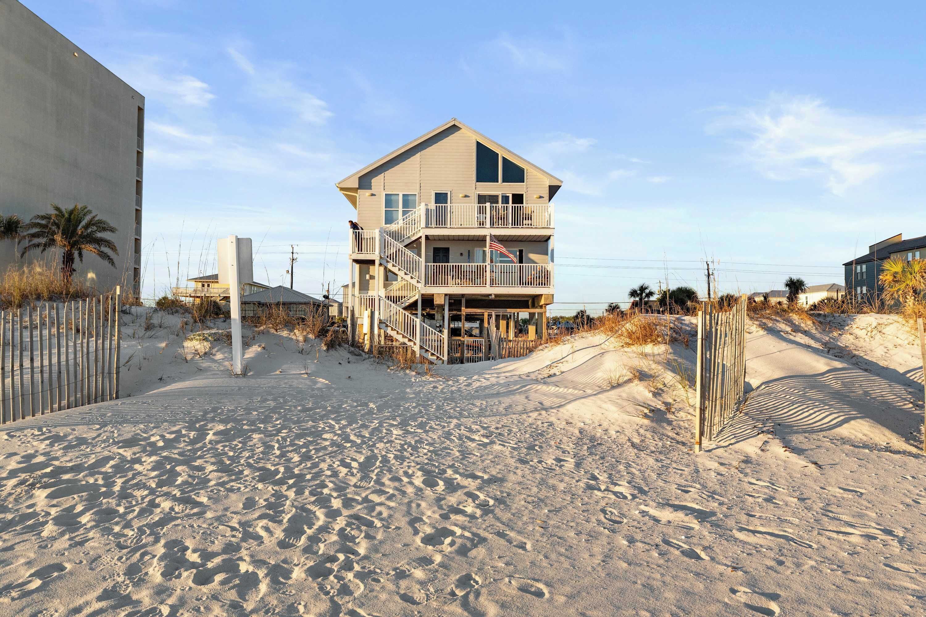 Una proprietà fronte spiaggia con una casa a più livelli, una spiaggia sabbiosa e un'area recintata.
