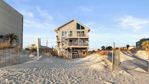 Une propriété située en bord de mer, comprenant une maison à plusieurs niveaux, une plage de sable et un espace clôturé.