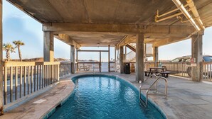 Une piscine extérieure située sous une structure en béton, agrémentée de garde-corps, de bancs et offrant une vue sur la plage.