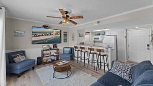 Un salon doté d’un ventilateur de plafond, d’un grand tableau, d’un coin bar avec des tabourets et d’un canapé.