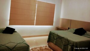 Een slaapkamer met twee bedden, een raam met zonwering, een airconditioning en een klein vloerkleed.