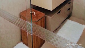 Een moderne badkamer met een douchecabine van glas, een beige wastafelmeubel en een klein houten krukje.