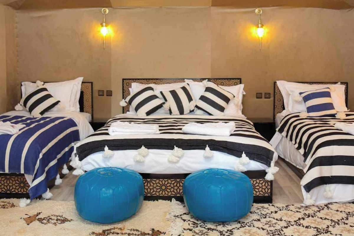 A bedroom with two beds, each with striped bedding and decorative pillows, a patterned rug, and two wall-mounted lights.