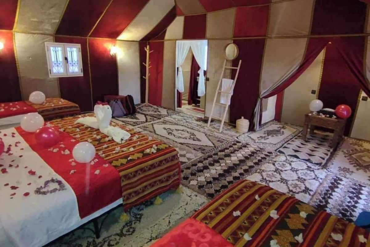 A tent-style room with multiple beds, a chandelier, and patterned rugs.