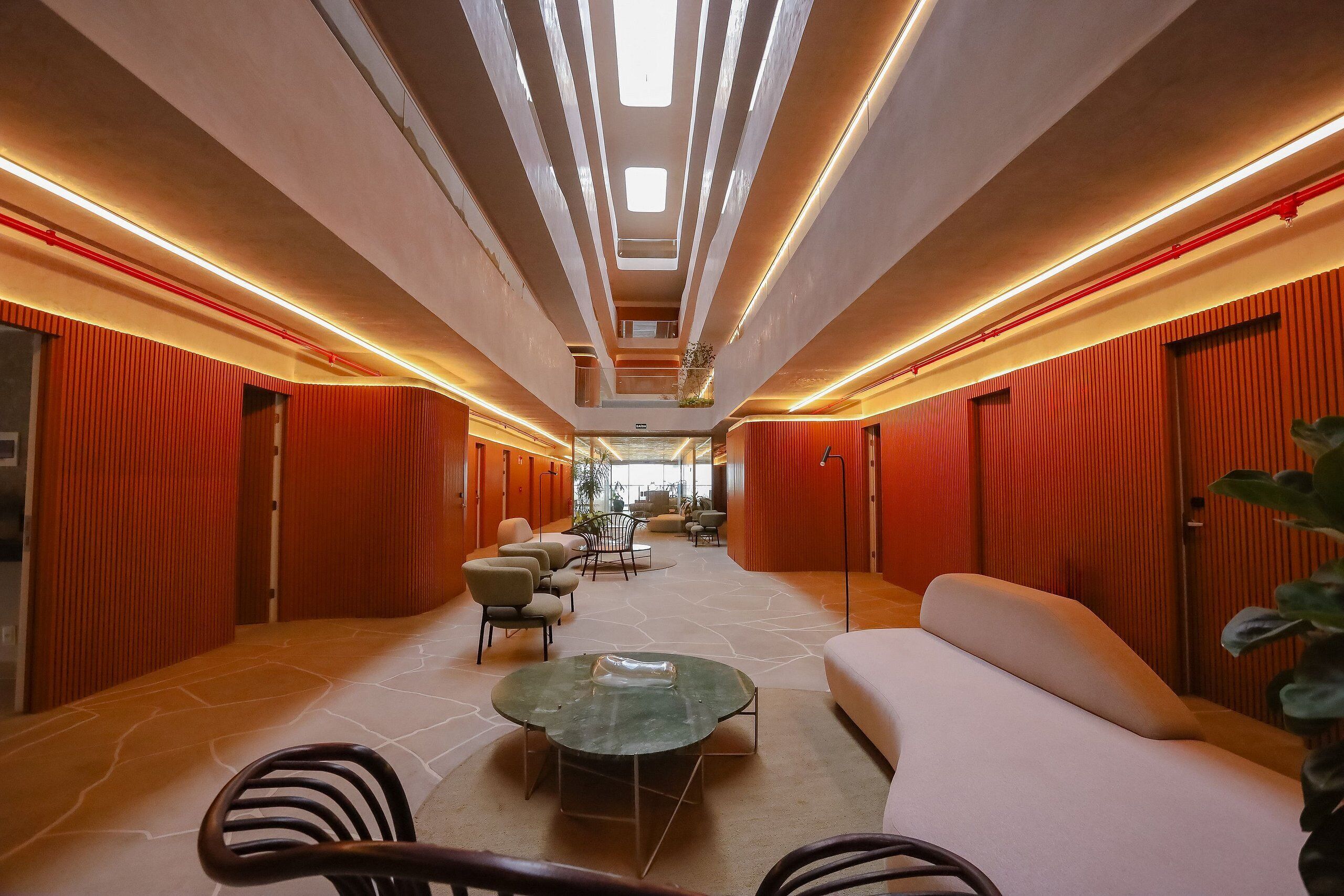 A modern hotel lobby with a central seating area, a staircase, and a view of the lobby in the background.