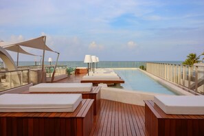 Ein Poolbereich mit Holzliegen und Blick auf den Ozean.
