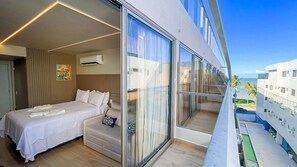 Una habitación de hotel moderna con una cama grande, un sofá y un balcón con vistas al océano y palmeras.
