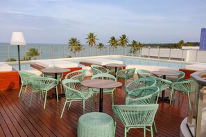 Zona de piscina en la azotea con sillas y mesas de mimbre verde, con vistas al mar.