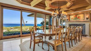 Ein Esszimmer mit einem großen, ovalen Tisch, Holzsesseln und Blick auf das Meer durch große Fenster.