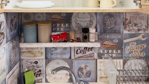 A compact kitchen with a sink, a stove, and shelves above holding various kitchenware.