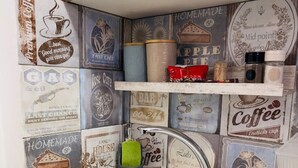 A kitchen with a stainless steel sink, a green sponge, and vintage coffee-themed wall decor.