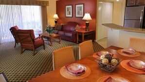 A hotel room with a dining area, a living room with a sofa and armchairs, a kitchen with a refrigerator, and a window with blinds. - Charming 2-bdrm villa in Lake Buena Vista, Florida near all family attractions. (Lake Buena Vista)