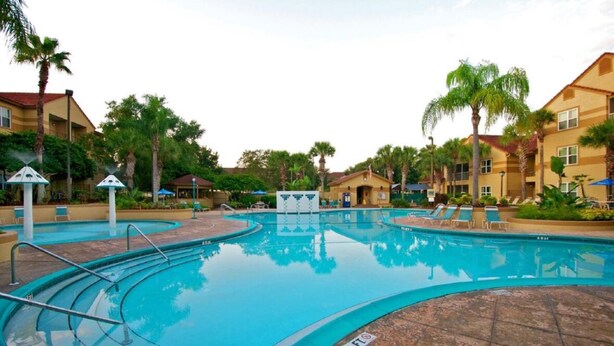 A swimming pool with multiple lanes, surrounded by palm trees and a building with a red roof. - Charming 2-bdrm villa in Lake Buena Vista, Florida near all family attractions. (Lake Buena Vista)