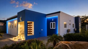 A modern house with a blue facade, a visible entrance, and a well-lit interior. - Modern 3-bedroom villa with private pool, great alarm system, WiFi, hot water! (Noord)