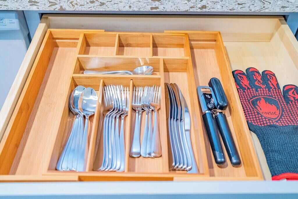 A drawer with neatly organized cutlery, including forks, knives, and spoons, and a pair of gloves.