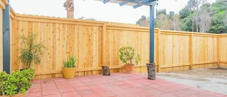 Un área de patio techada con cerca de madera, plantas en macetas y piso de baldosas.