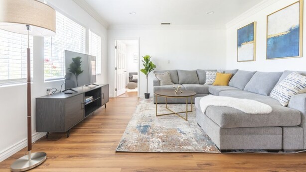 Een moderne woonkamer met een grijze bank, een ronde salontafel en een tv op een kast.