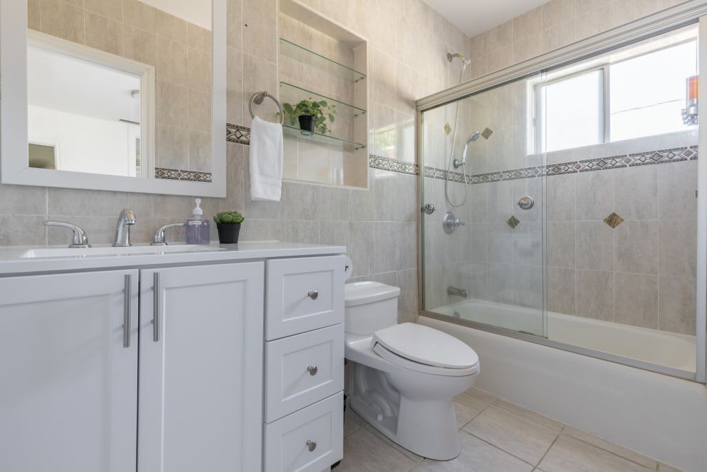 A modern bathroom with a glass-enclosed shower, a white toilet, and a vanity with drawers and a mirror.