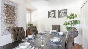 Een eetkamer met een donker houten tafel voor zes personen, omringd door zes grijze gestoffeerde stoelen.