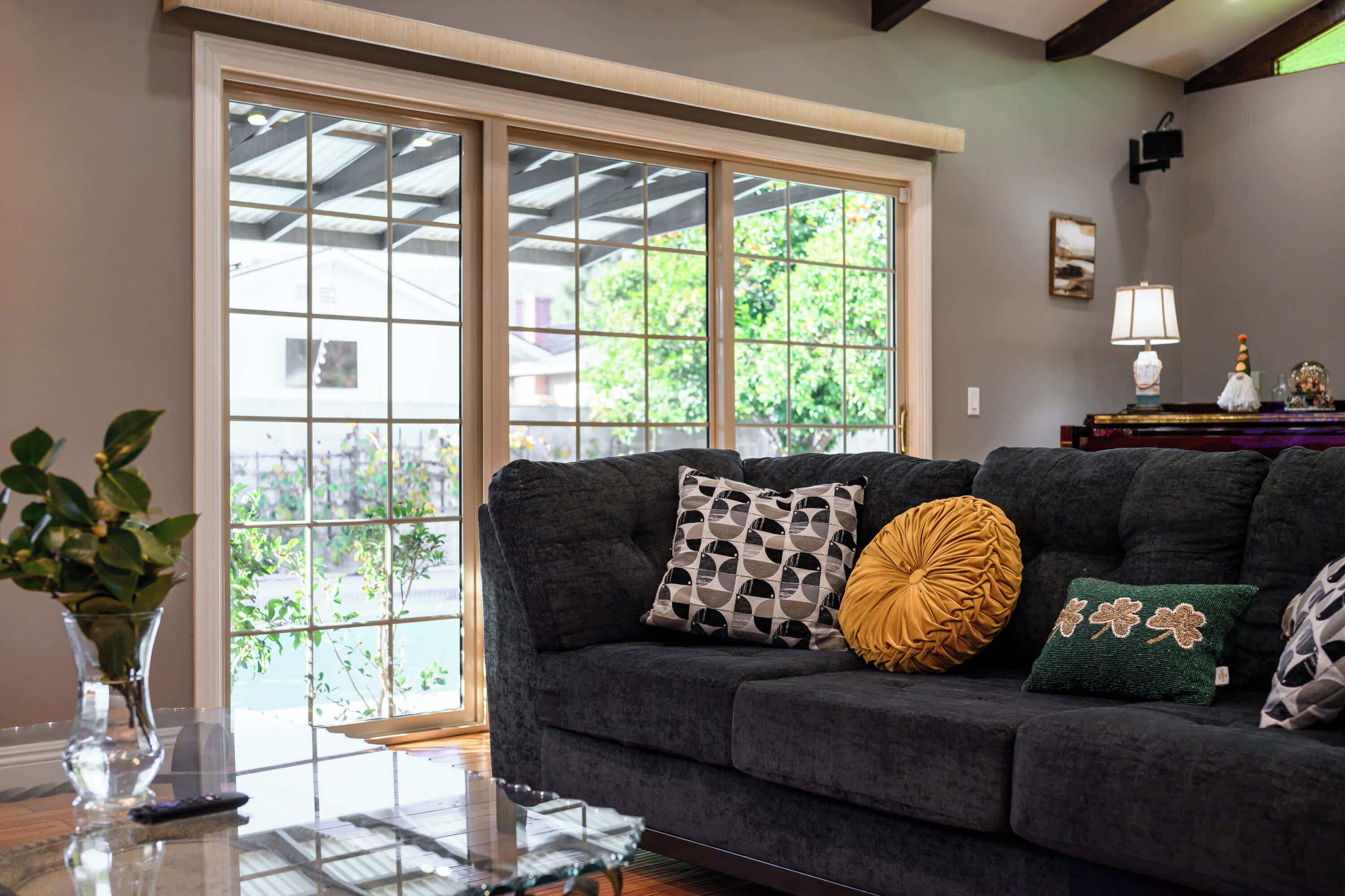 A living room with a dark grey sofa, a glass coffee table, and a vase with green plants.
