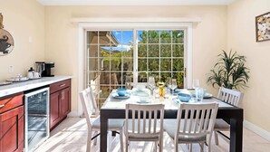 Una cocina con comedor, que cuenta con un amplio ventanal, un refrigerador y una mesa de comedor servida con platos y vasos.