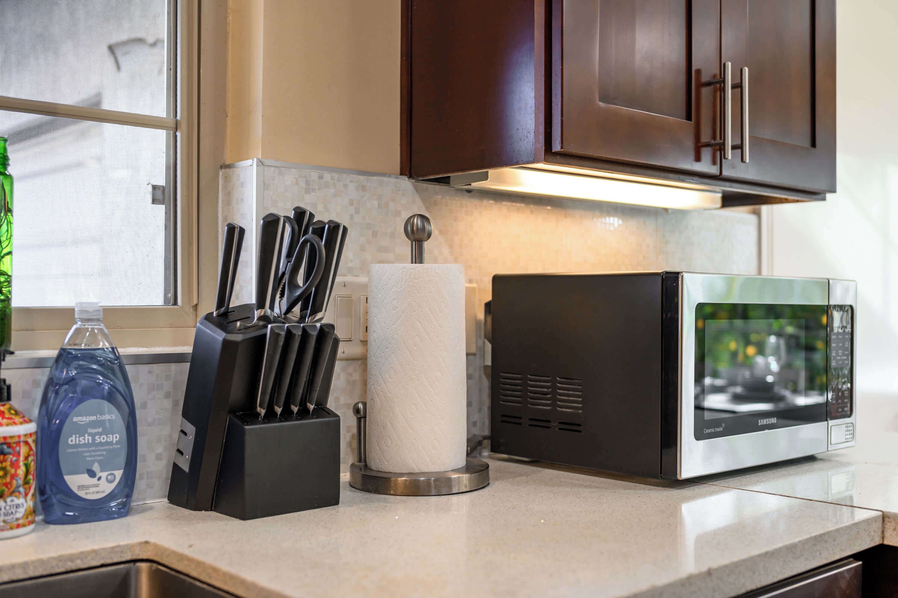 A kitchen with a microwave, a dish soap bottle, a knife block, and a paper towel holder.
