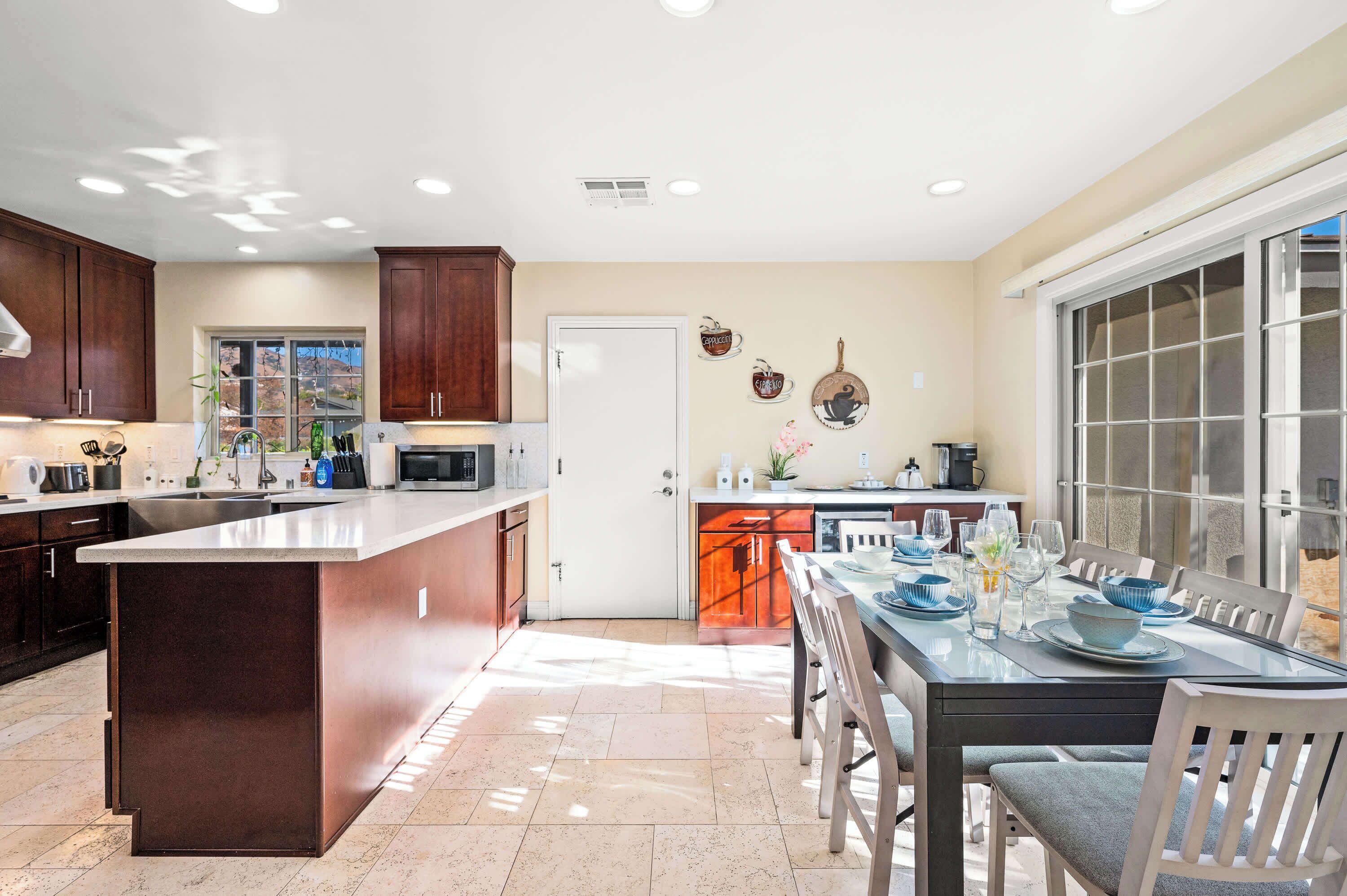 A modern kitchen with a central island, a dining area with a table set for four, and a large window providing natural light.