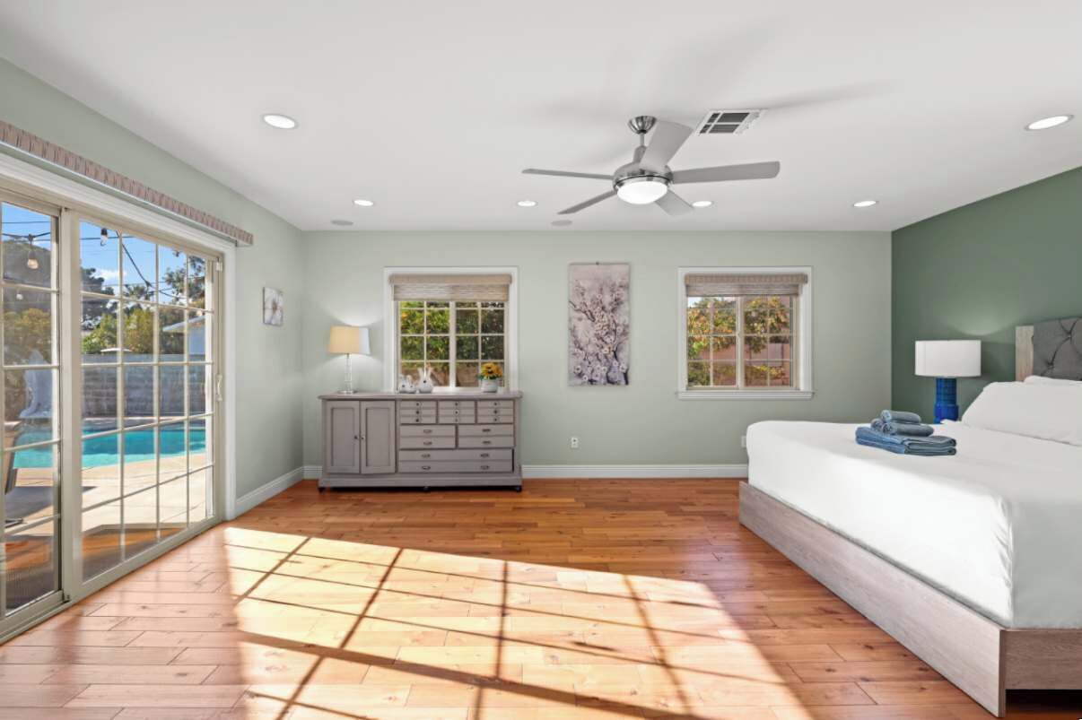 A bedroom with a large bed, a ceiling fan, and a view of a swimming pool through a sliding glass door.