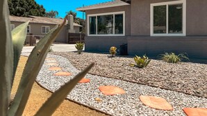 A modern house with a paved driveway, a small garden with plants, and a clear blue sky. - Cozy 2BR Home With Bright Interior & Relaxing Patio (Ontario)