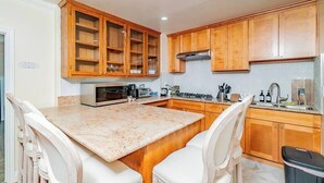 A kitchen with wooden cabinets, a granite countertop, a microwave, a stove, and a sink. - Monterey Park Retreat: Spectacular Views & Comfort (Monterey Park)