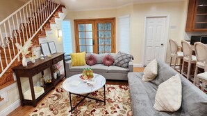 A living room with a staircase, a gray sofa, a white coffee table, and a patterned rug. - Monterey Park Retreat: Spectacular Views & Comfort (Monterey Park)