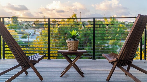 A wooden deck with two chairs and a table, a wicker basket with a plant, and a view of greenery and a cloudy sky. - Monterey Park Retreat: Spectacular Views & Comfort (Monterey Park)