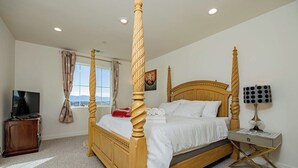A four-poster bed with a wooden headboard, a bedside table with a lamp, and a television on a wooden cabinet. - Luxurious Ontario Townhouse: Ideal Family Retreat (Ontario)