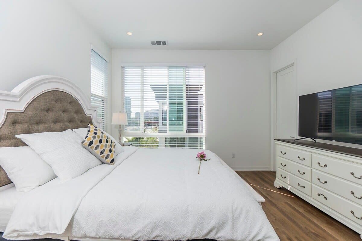 Quarto com cama, penteadeira, televisão e janela com persianas.