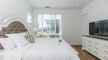 Quarto com cama, penteadeira, televisão e janela com persianas.