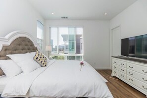Un dormitorio con cama, cómoda, televisor y ventana con persianas.