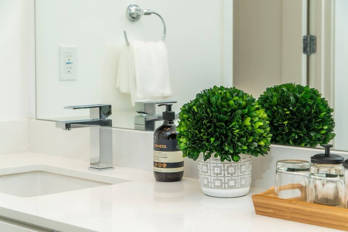 Een badkamer met een witte wastafel, een spiegel, een handdoekhouder en twee potplanten.