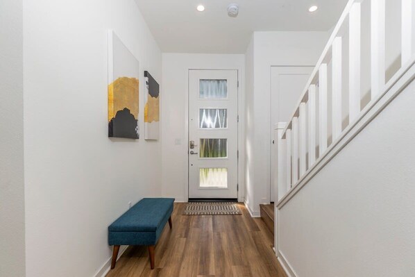 A hallway with a bench, a door with frosted glass panels, and a staircase with white railings. - Master Bedroom With King Bed Central Location (Irvine)