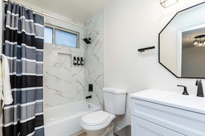 A bathroom with a bathtub, toilet, and a large mirror. There are toiletries on the wall and a shower curtain. - Not Affected by the Fire/elegant Pasadena Retreat Prime Comfort Awaits (Pasadena)