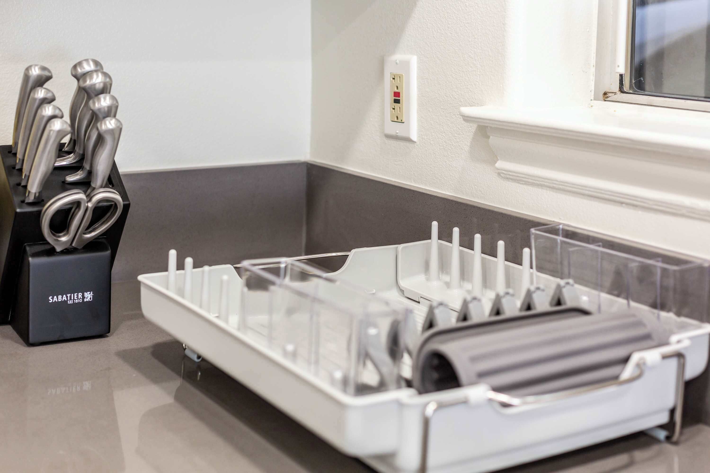 A kitchen area with a dish rack, a knife block, and a power outlet on the wall.