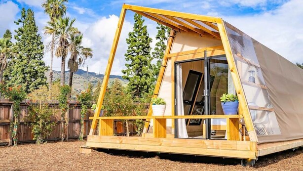 A small, triangular, wooden structure with a glass door, surrounded by a wooden fence and trees. - Urban Glamping Oasis: Comfort & Adventure Combined (Glendora)