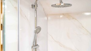 A shower with a handheld showerhead and a fixed overhead showerhead in a bathroom with marble walls. - Urban Glamping Oasis: Comfort & Adventure Combined (Glendora)